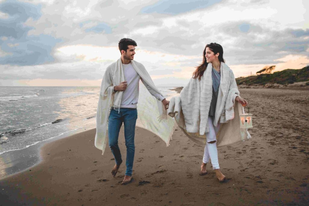 A couple walk hand in hand toward the photographer on a beach in Ayrshire