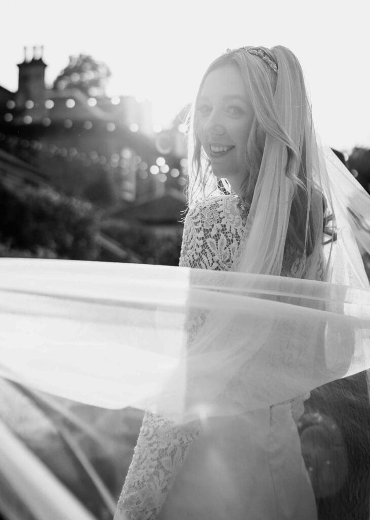 the bride smiles at the camera with teh sun backlighting her in the gardens in Glasgow
